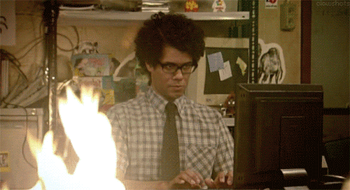 Moss from IT Crowd typing on the computer while a fire is in front of him